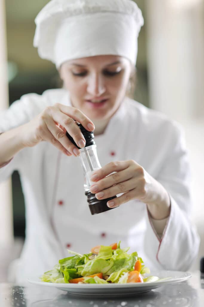 Bella Hartte seasoning a fresh salad with a pepper grinder